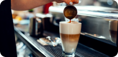 Fresh espresso pours from a commercial coffee machine into a glass latte, creating distinct layers of milk and coffee.