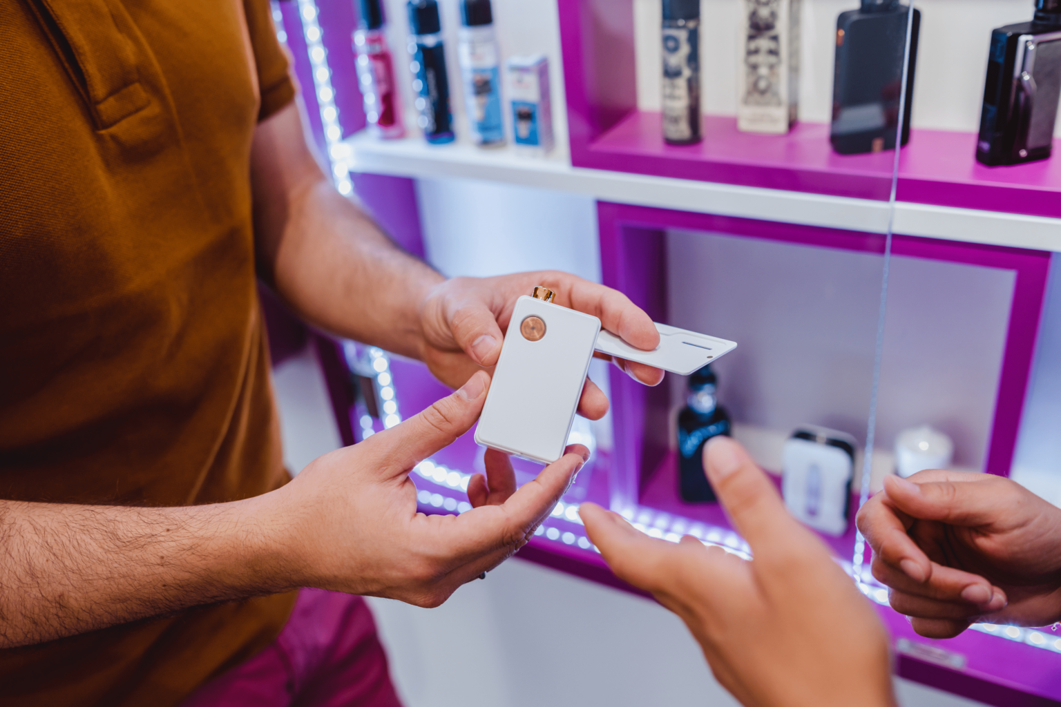 Close-up of hands holding a packaged retail product while browsing a display case, with illuminated shelves and merchandise visible.