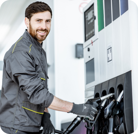 Person in gray work uniform operating fuel pump nozzle at a modern gas station with multiple dispensers.