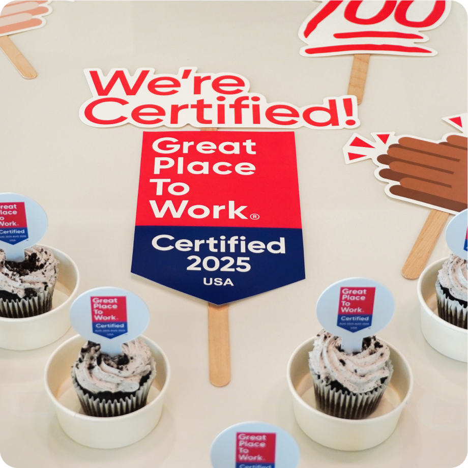 Employees display Great Place to Work Certified 2025 signs and celebration props while participating in an office event.