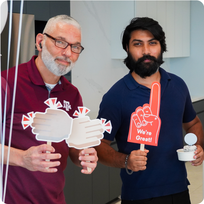 Two Modisoft team members hold workplace celebration props and branded cupcakes during a Great Place to Work certification event.