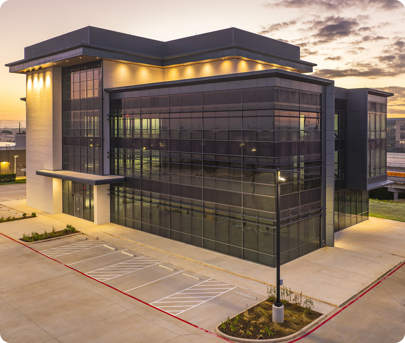 Exterior view of the Modisoft headquarters featuring a modern glass office building with illuminated architectural details and surrounding parking area.