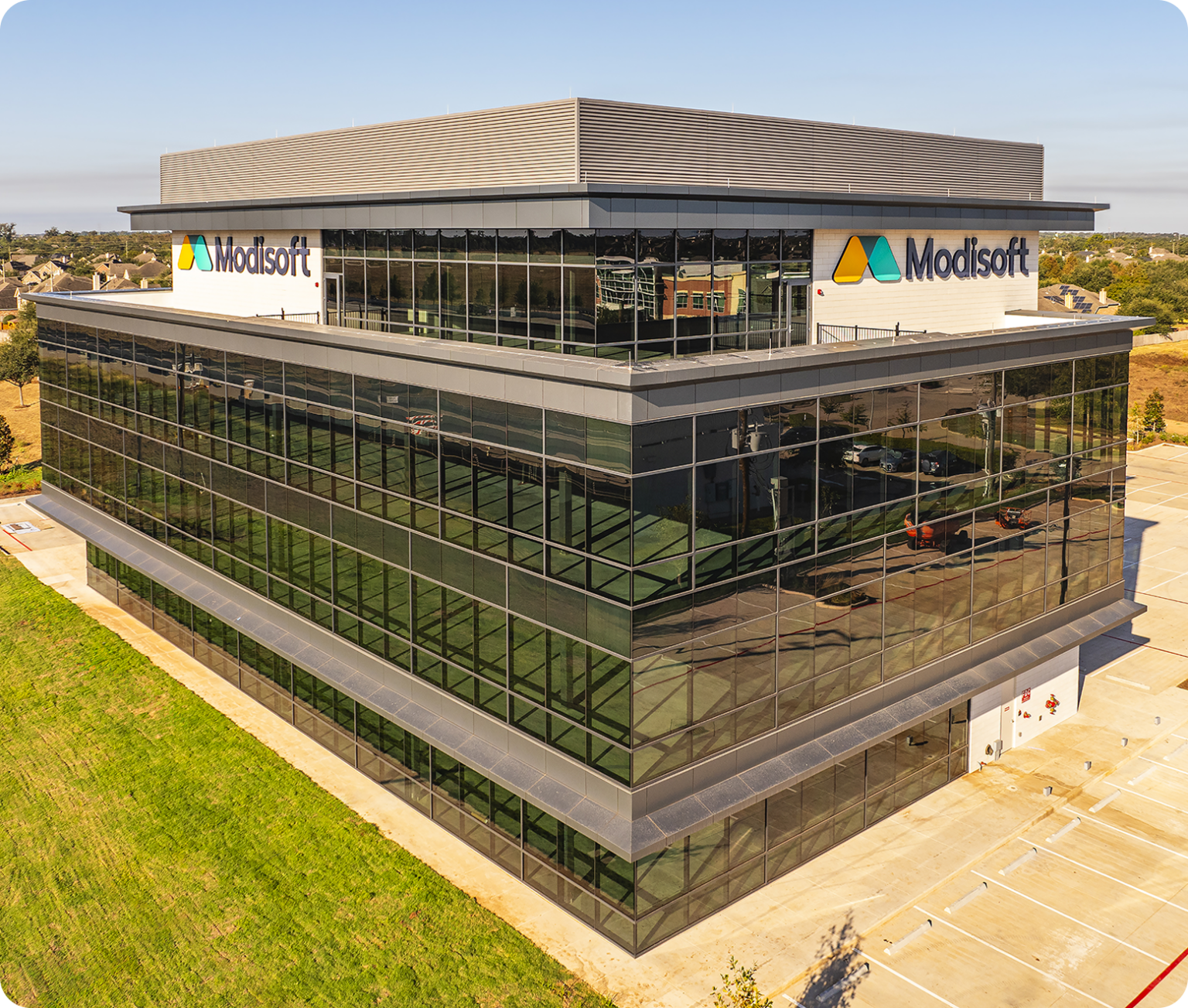 Aerial view of the Modisoft office building with glass exteriors, company logo, surrounding parking areas, and landscaping.