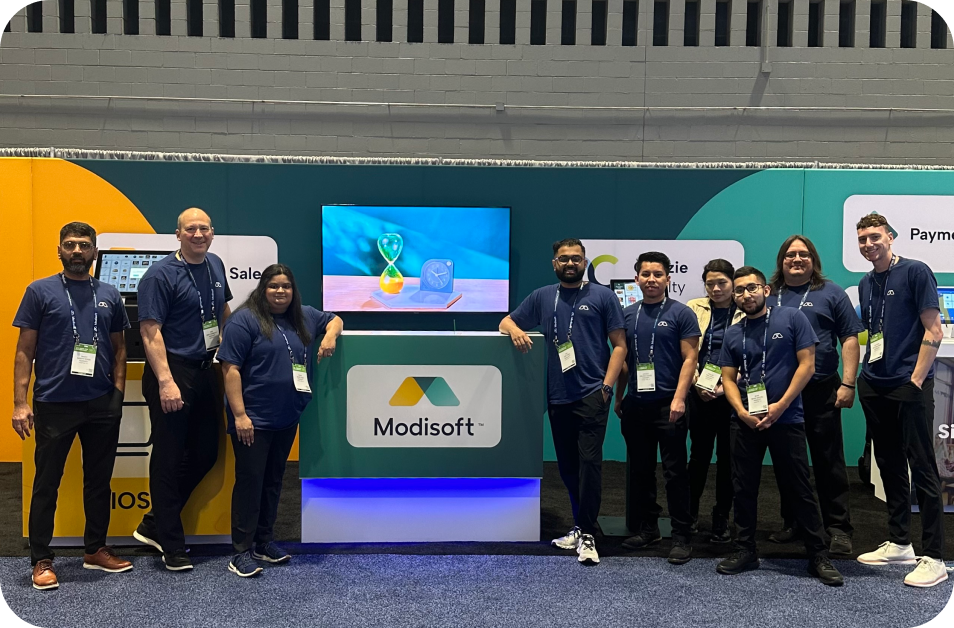 Modisoft team members standing at a branded trade show exhibit booth featuring company signage, display screens, and business technology solutions.
