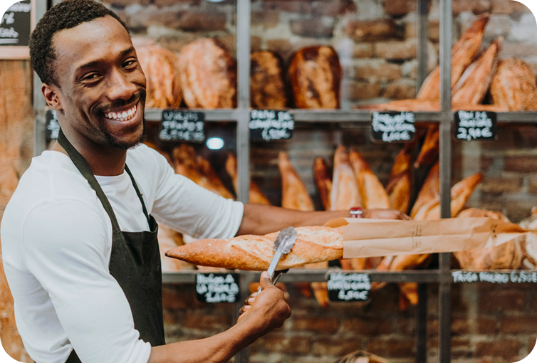 Bakery employee arranging freshly baked bread in front of artisan loaf displays and bakery shelving.