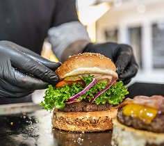 Food preparation scene showing a burger being assembled with lettuce, onions, and toppings.