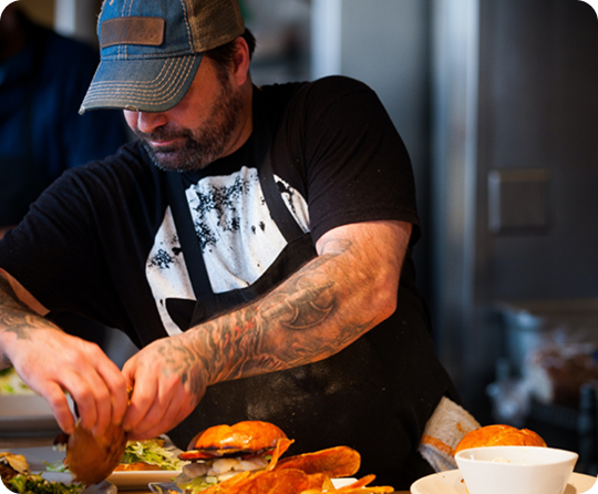 Kitchen staff member preparing burgers and food orders at a fast casual restaurant cooking station.