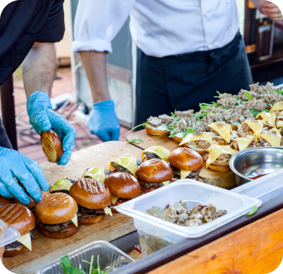 Food service staff preparing multiple burger orders at a fast food kitchen workstation during peak service hours.