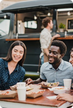 Guests seated at an outdoor dining table with food and beverages beside a mobile food service station.
