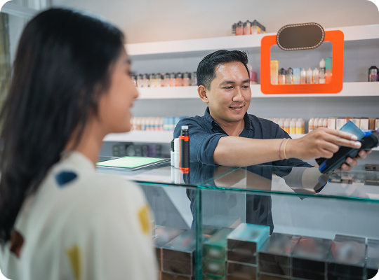Customer completing a payment transaction at a smoke shop checkout counter with tobacco and vape products displayed on shelves in the background.
